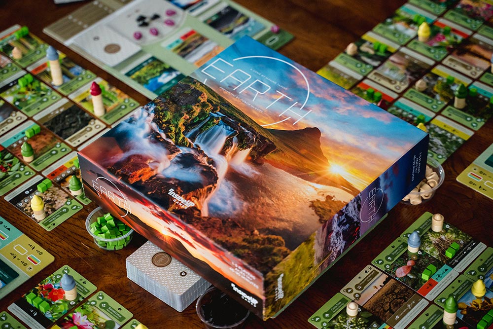 The box for the Earth board game surrounded by its cards and playing pieces