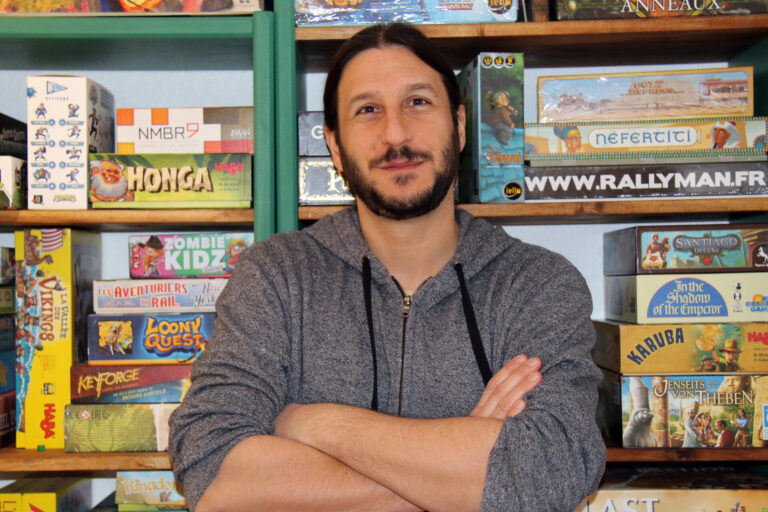 Board game designer Antoine Bauza sits in front of shelves full of games